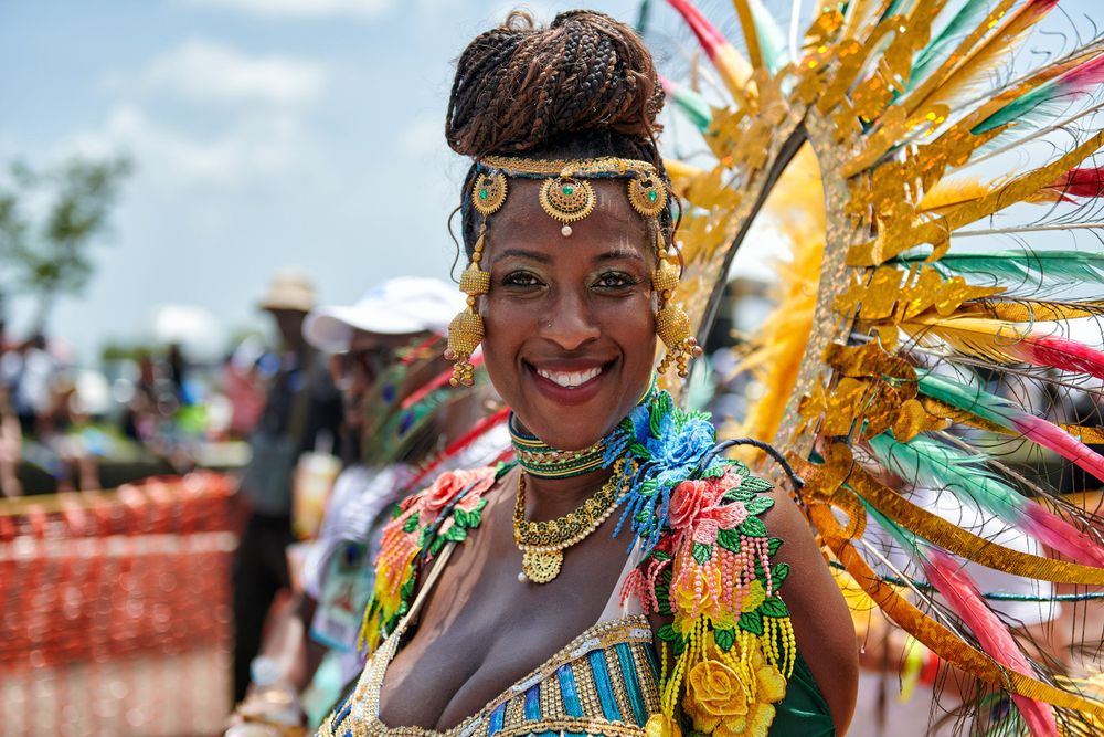 Vibrant carnival performer wearing colorful feathered headdress and festive jewelry at outdoor festival.