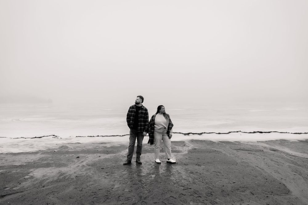 Two people walk together along a misty beach shoreline in black and white.