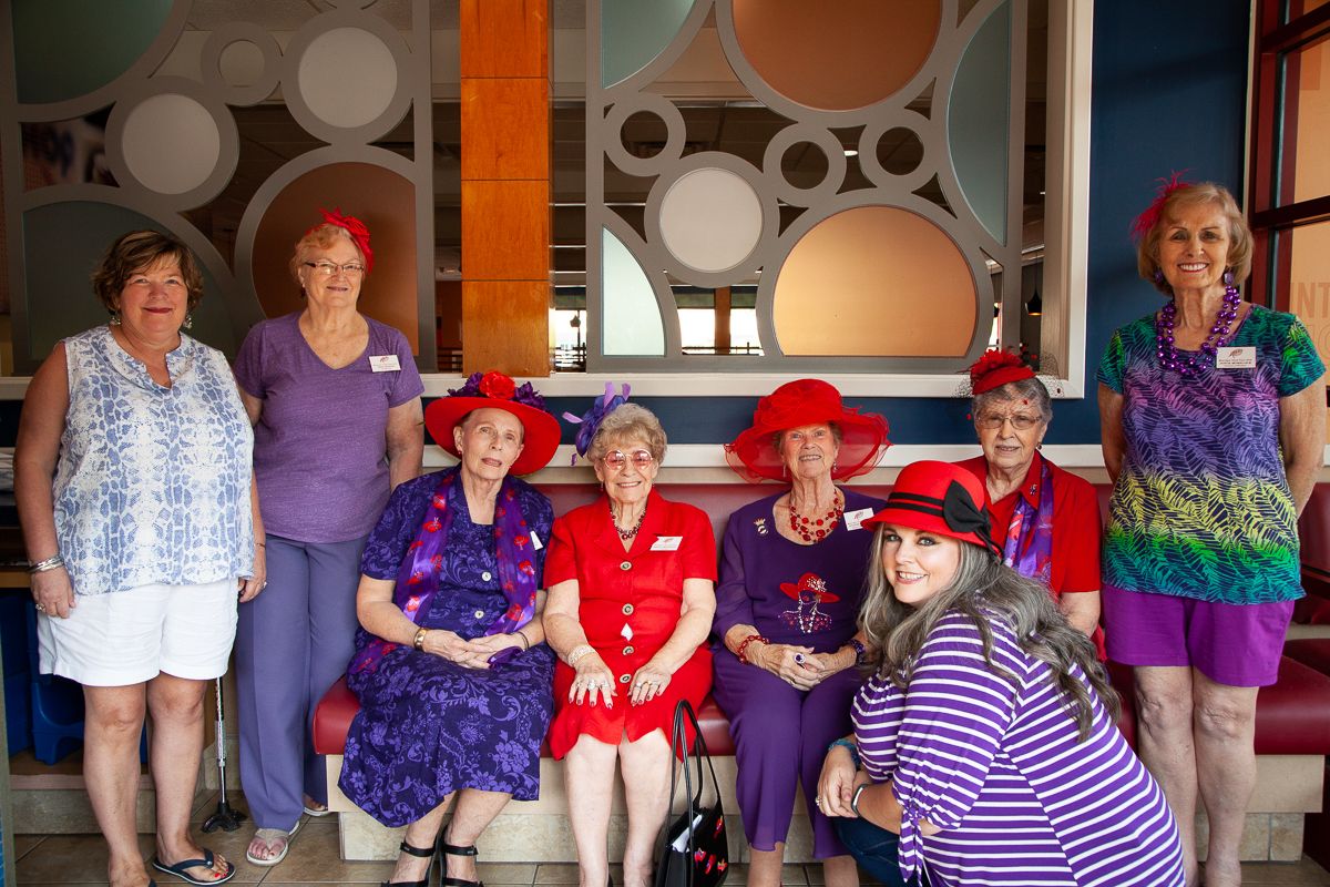 Group wearing coordinated purple and red outfits poses together against retro circle backdrop.