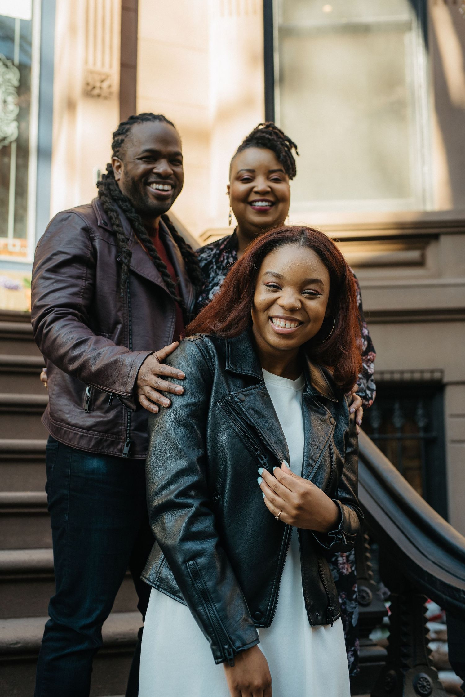 Three people sharing laughter and embraces on urban brownstone steps.