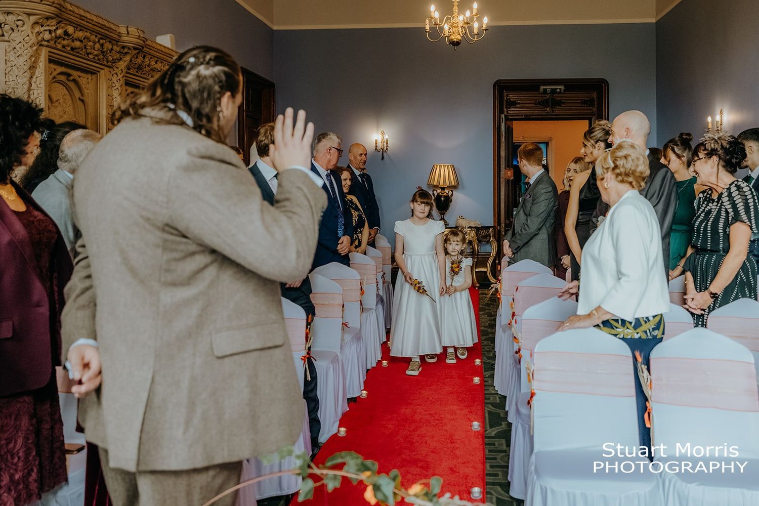 groom waves to the flower girls walking down the aisle at ruthin castle Stuart Morris Photography