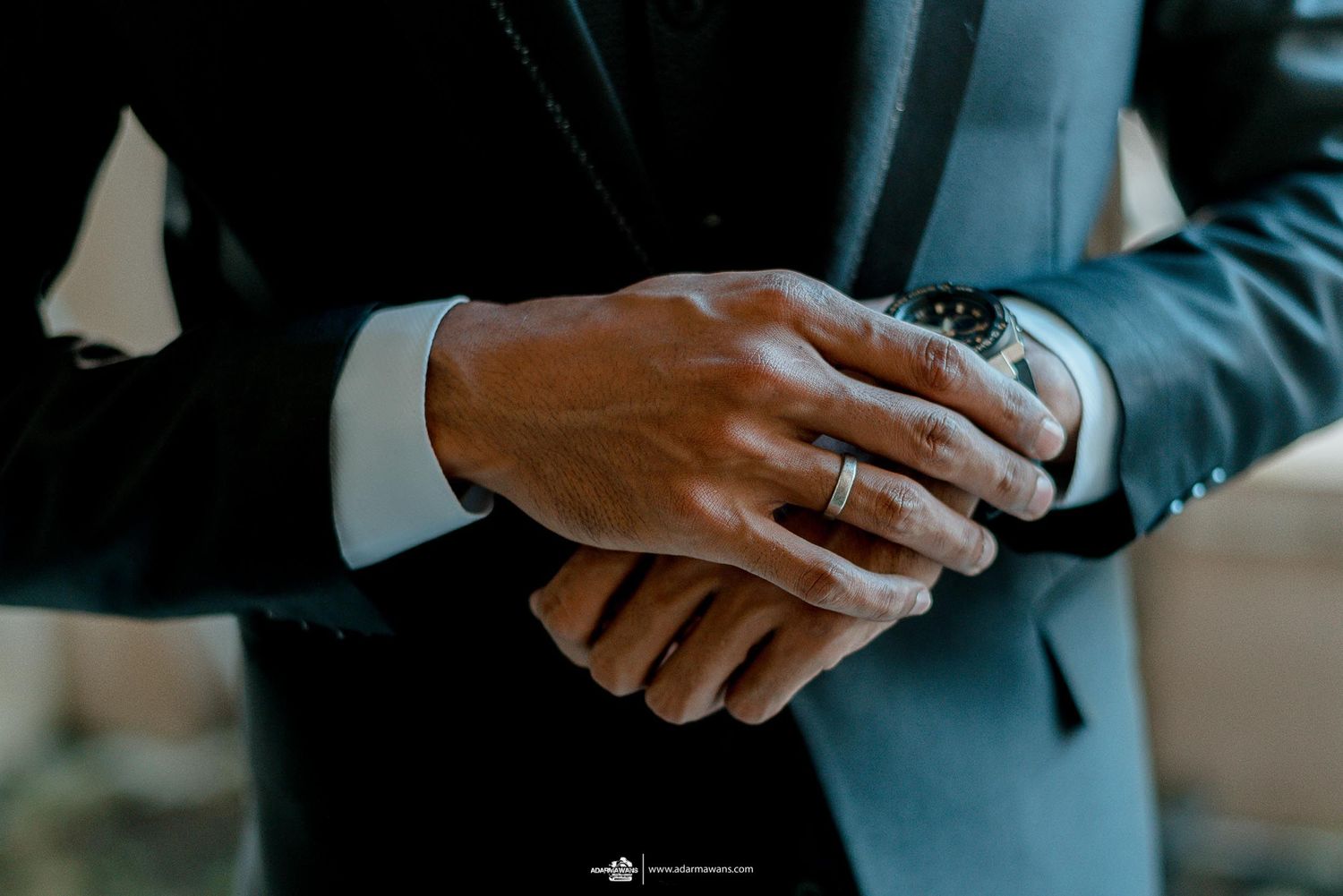 Groom's hands crossed showing wedding ring detail against dark suit.