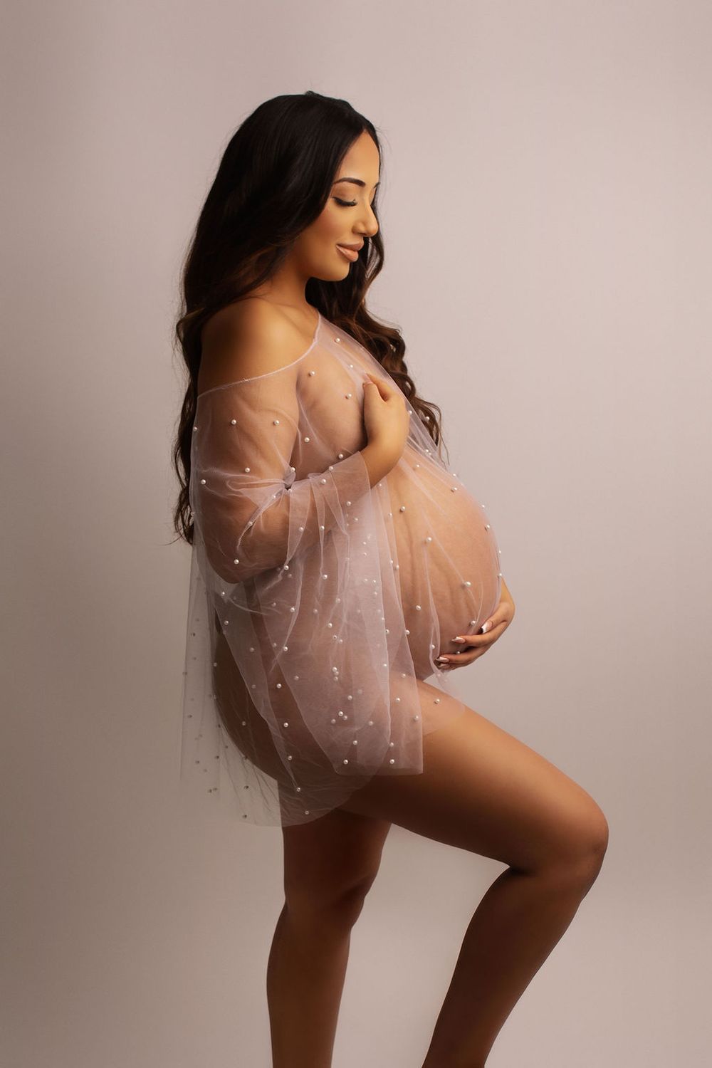 Artistic maternity photo with sheer flowy dress against pink background showing silhouette and curves.