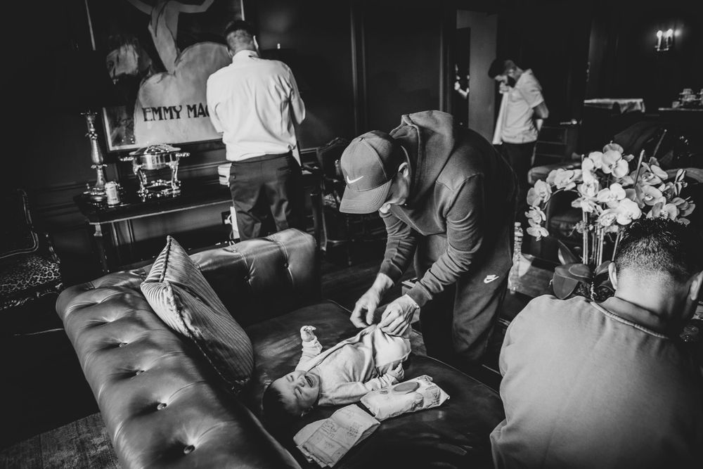 Black and white candid moment at a party venue with guests relaxing on a tufted leather couch in a dimly lit atmosphere.