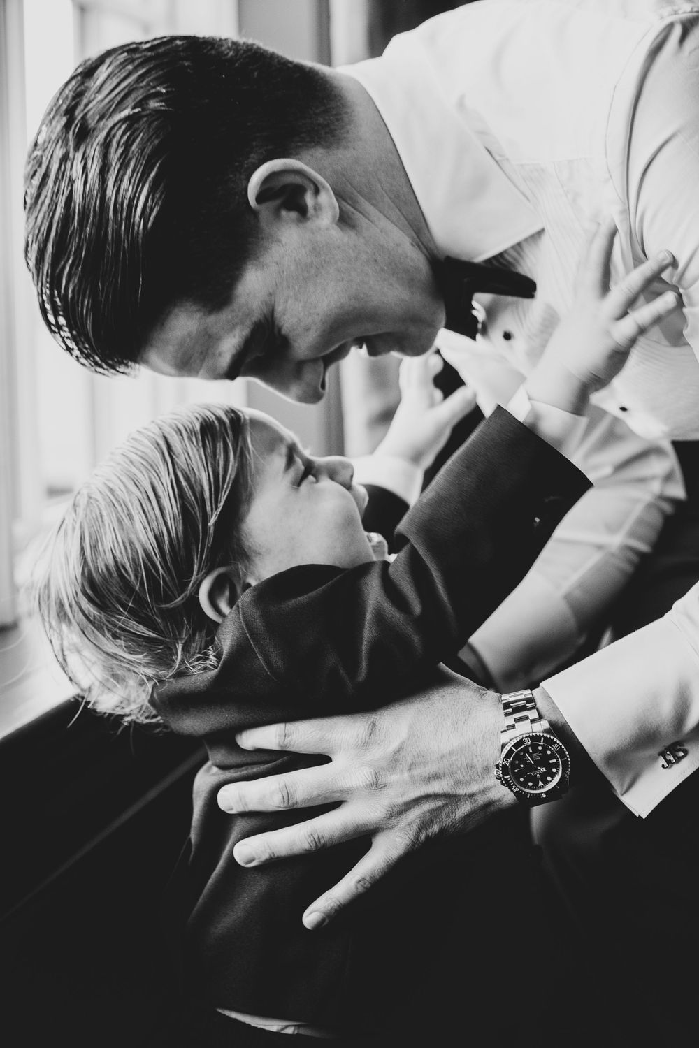 A black and white image shows an intimate moment between a parent and child in formal attire.