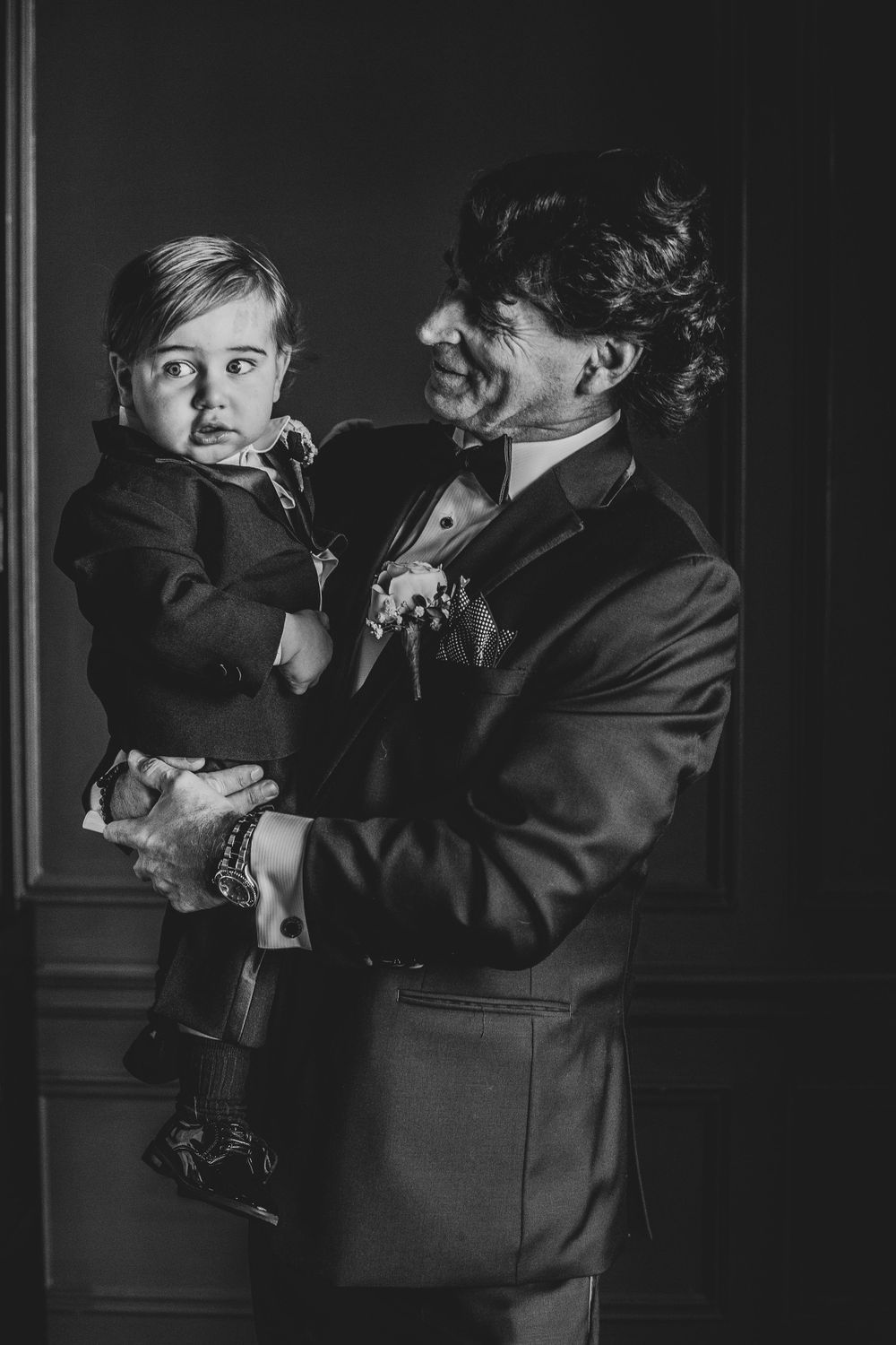 Black and white portrait of a parent holding a young child captured in tender moment at formal event.