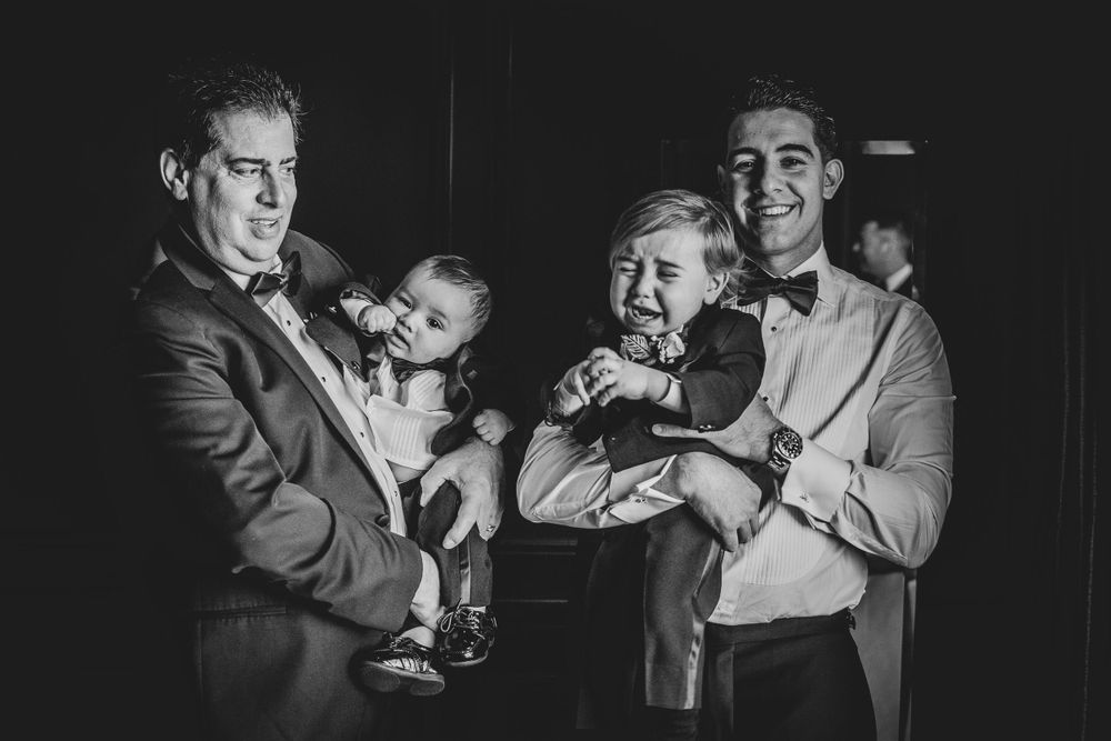 Black and white photo of well-dressed men holding happy babies at a formal event.