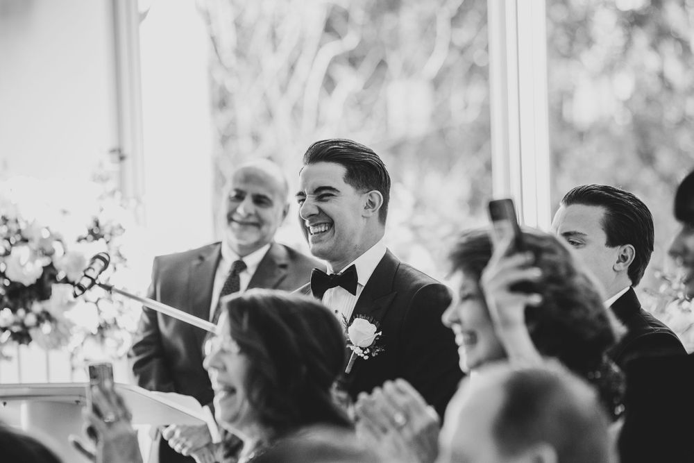 Black and white photo of groomsmen laughing and celebrating during wedding reception speeches.