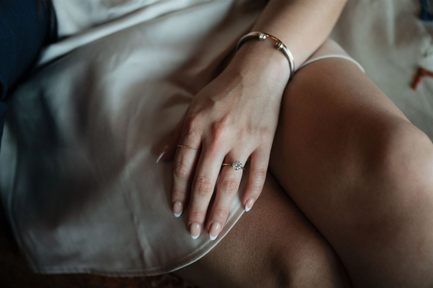 Close-up of hand with engagement ring resting on white dress fabric.