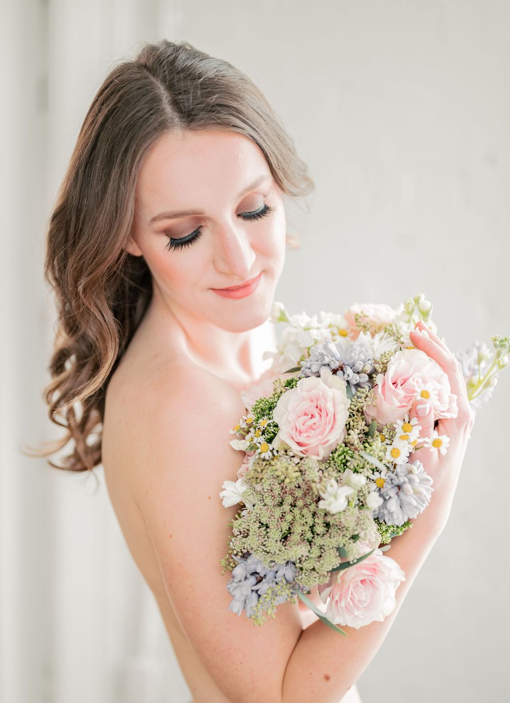 Delicate bridal bouquet with pink roses and white baby's breath held against light background.