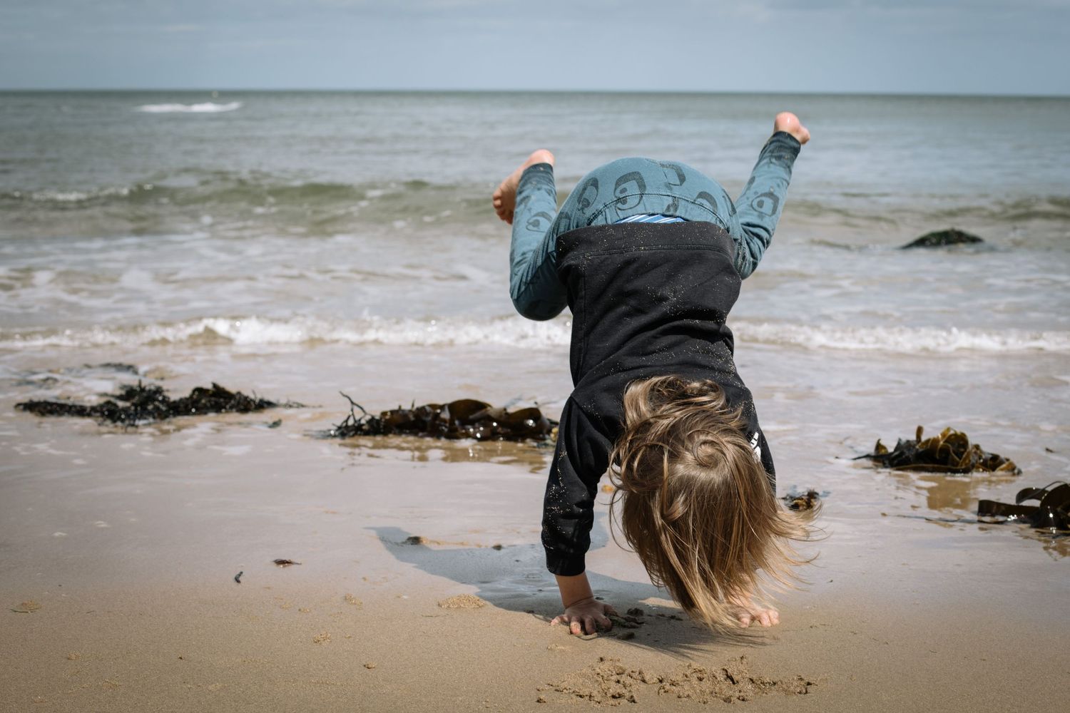 Person does a handstand on the beach with waves in the background.