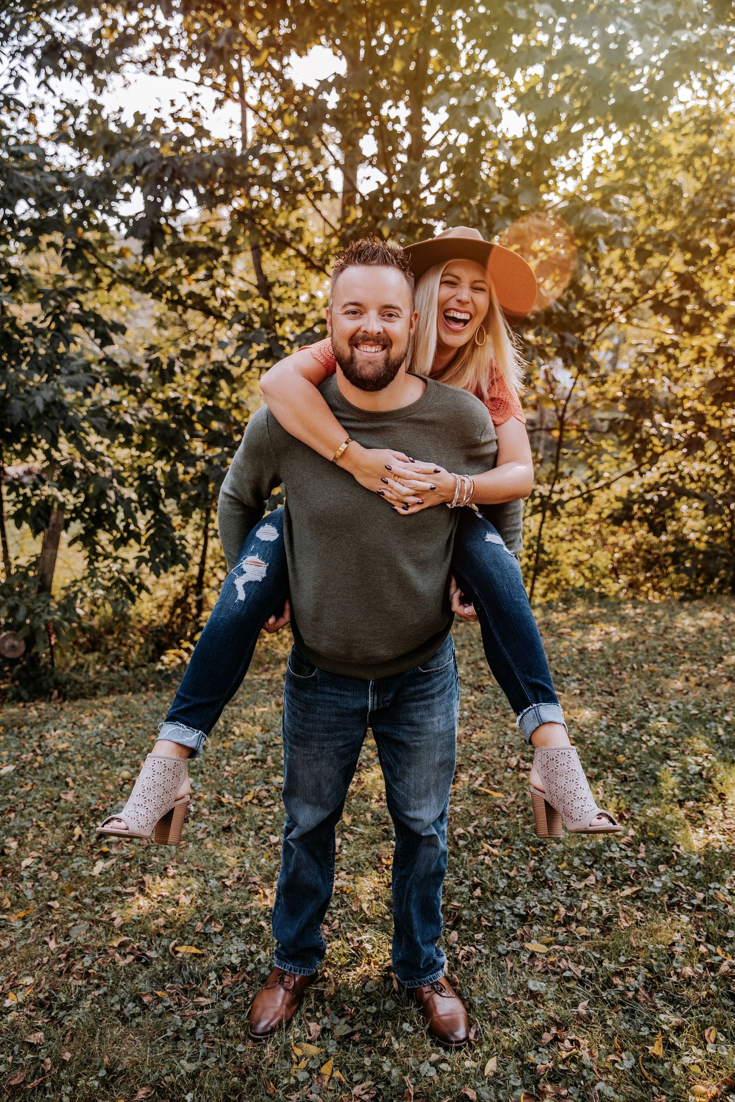 A playful couple enjoying a piggyback ride in a sunlit forest setting during autumn.