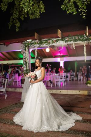 Bride in stunning white ball gown with long train poses outdoors at night under floral arch.