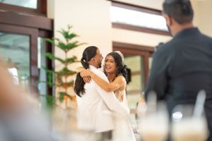 Smiling bride hugs guest warmly during wedding reception in bright modern venue.