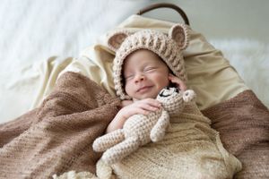 Newborn sleeping peacefully in cozy knit bear hat while holding plush toy.