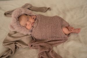 Sleeping baby wearing cozy pink hooded outfit on beige blanket.