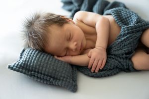 Sleeping infant on textured grey pillow wrapped in knit blanket.