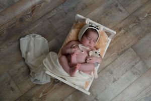 Newborn baby resting on white blanket against wooden floor background.