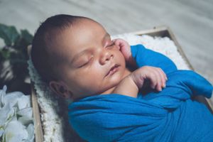 Sleeping newborn wrapped in soft blue fabric with white floral accents.