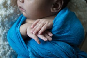 Close-up of sleeping newborn's hands wrapped in blue fabric.