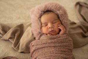 Baby sleeping in soft pink furry hood and brown wrap.