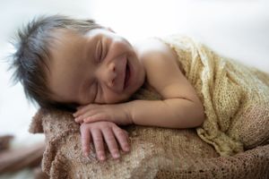 Baby sleeping on brown blanket with peaceful expression.