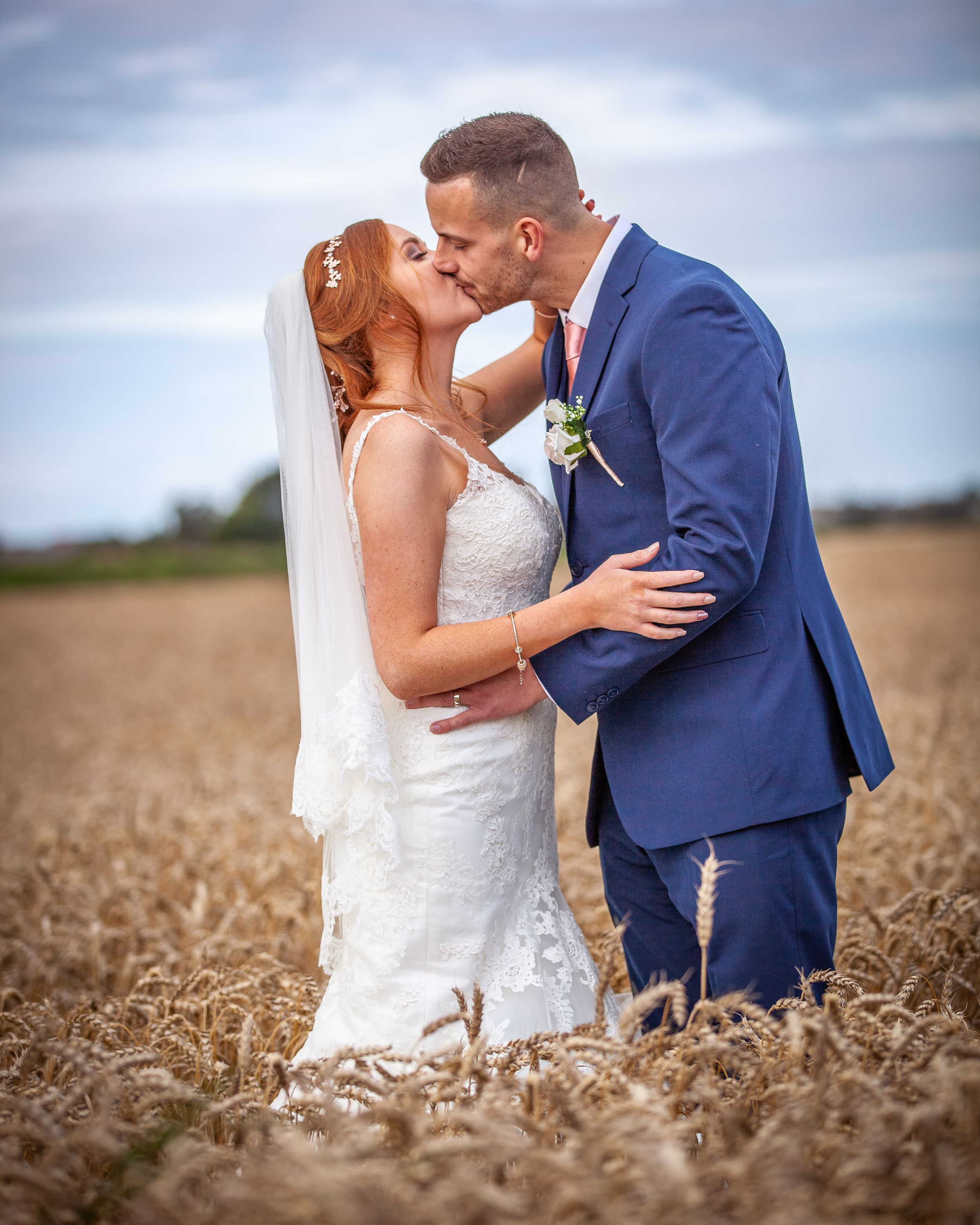 Bride and groom share a romantic kiss in a golden wheat field on their wedding day.