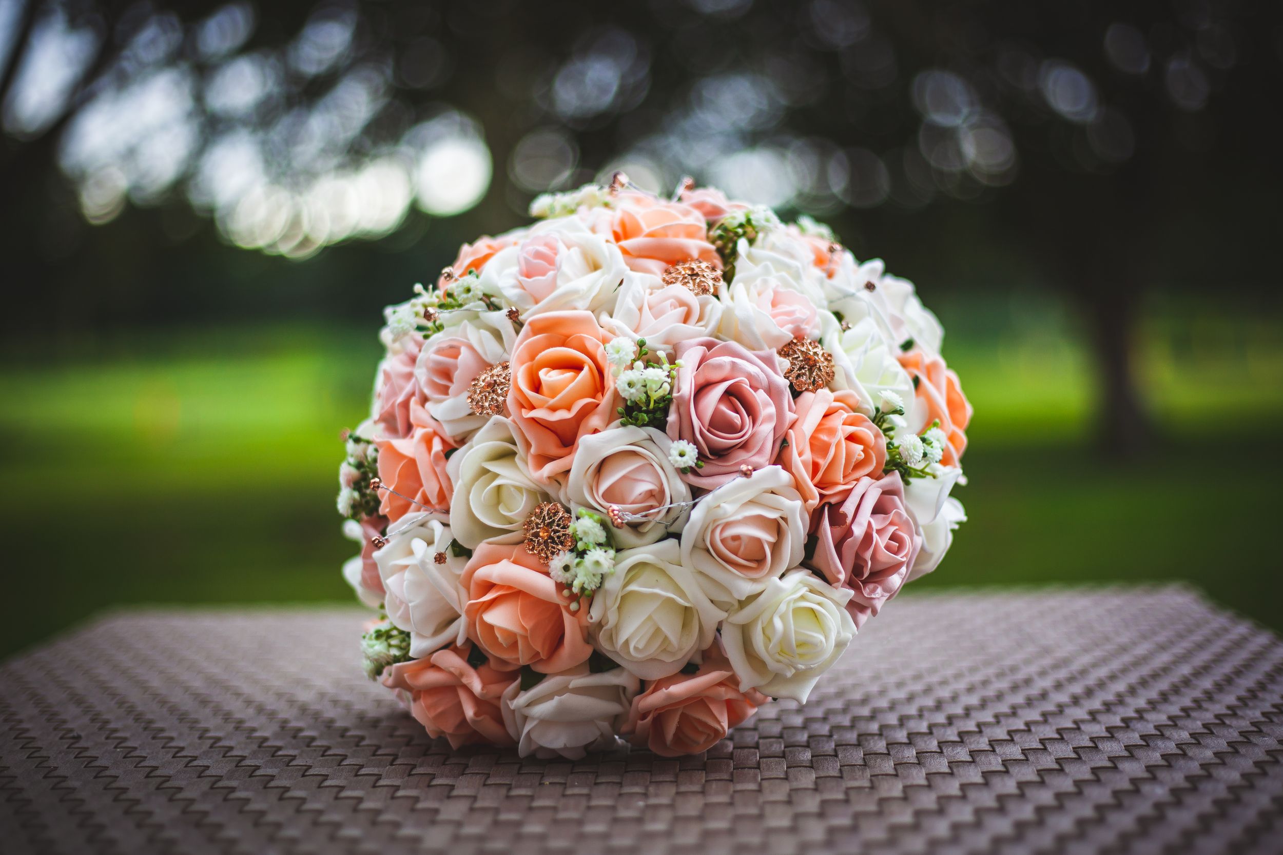 Beautiful bridal bouquet of peach and white roses arranged on wicker surface outdoors.