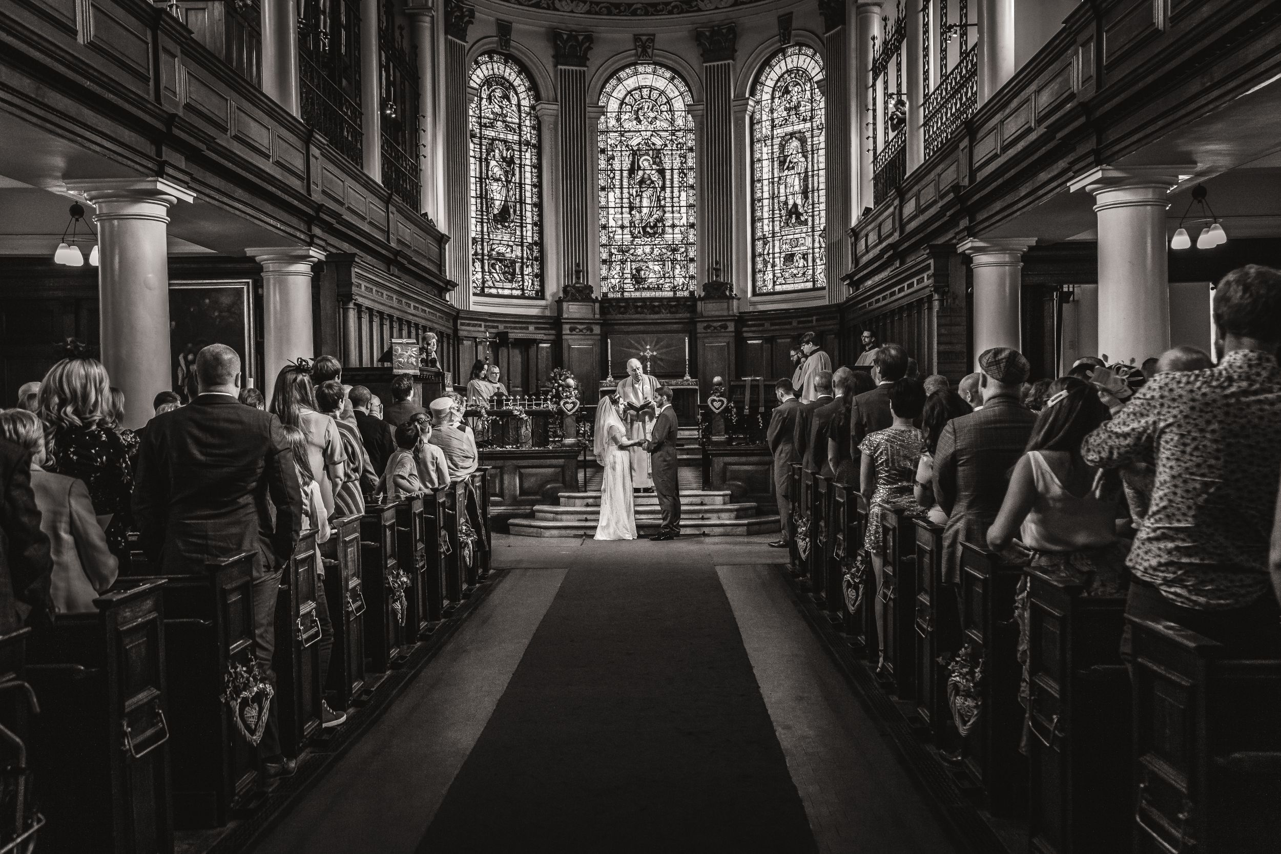 Black and white photo of a wedding ceremony inside an elegant church with stained glass windows.