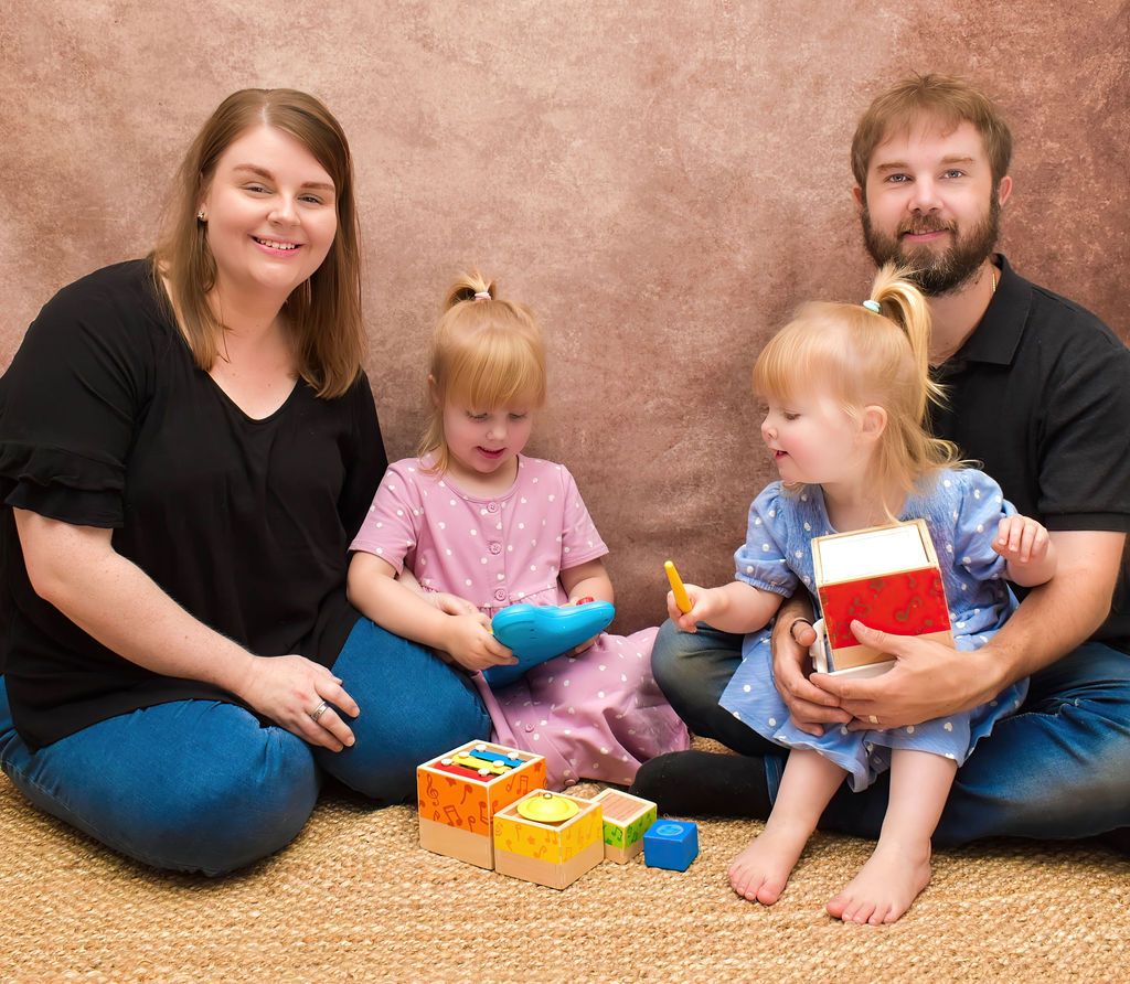 Family members sitting on carpet playing with colorful toys and blocks together.