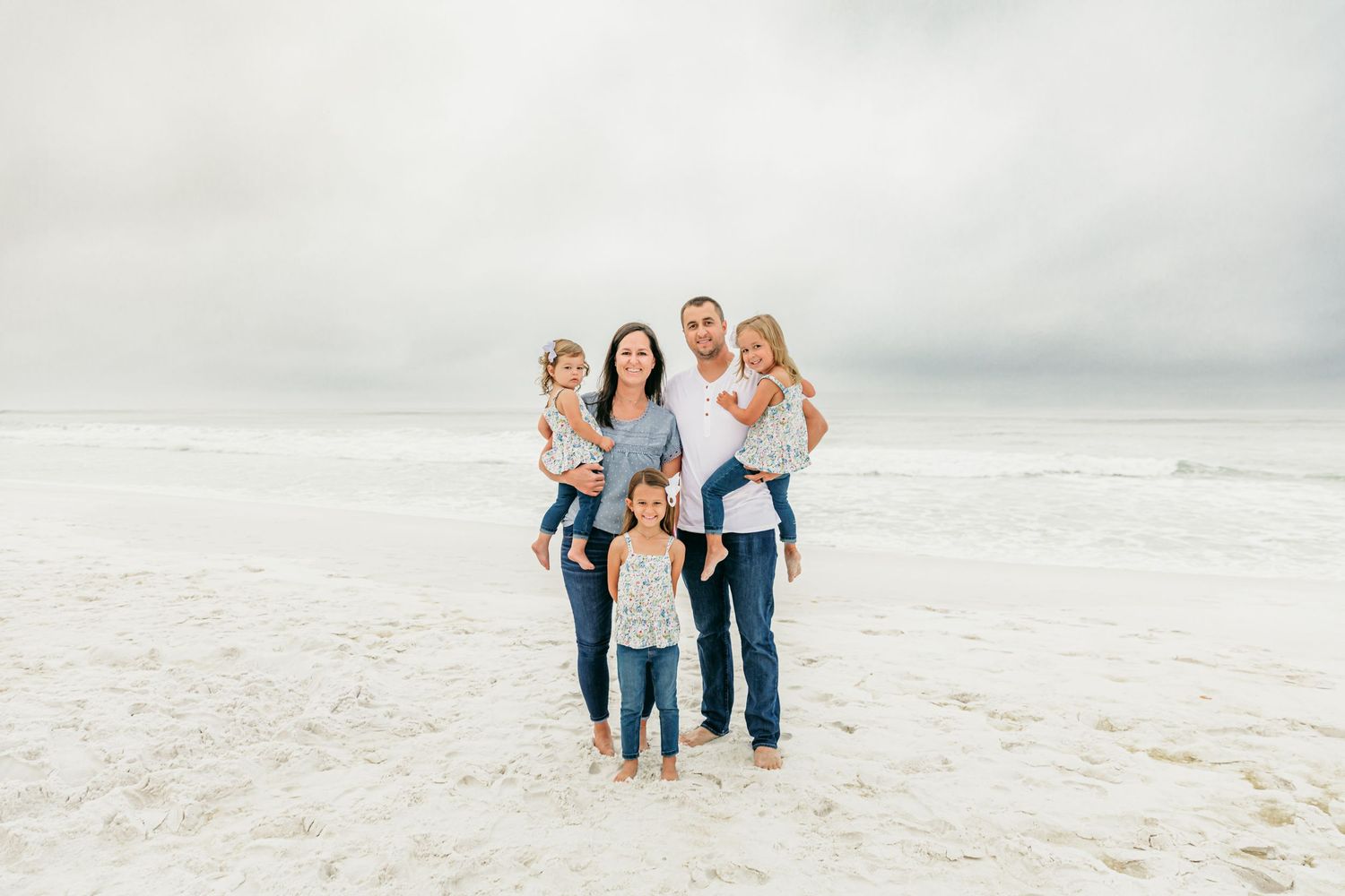 Family members walk together on a pristine white beach with waves crashing in the background.