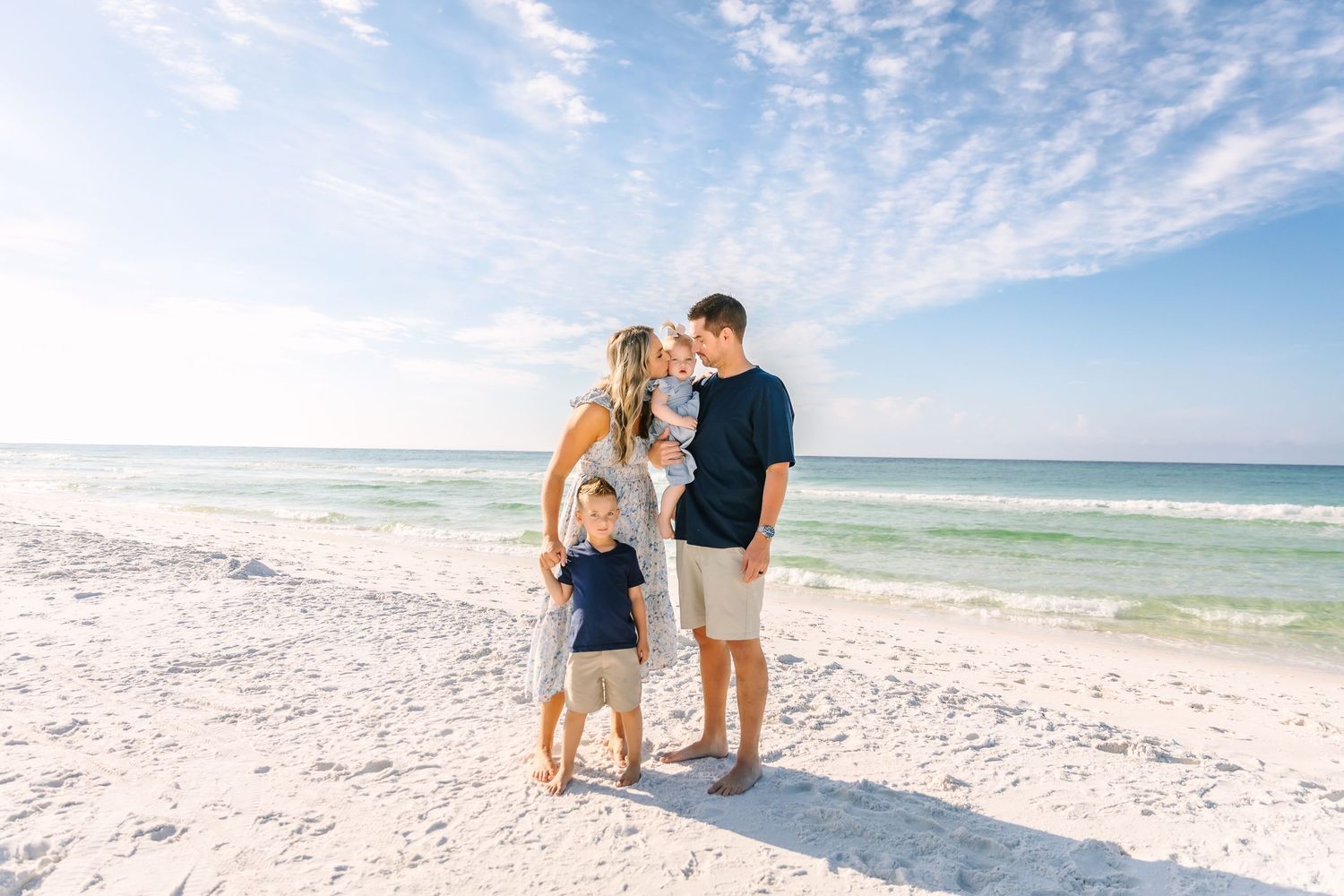 A beach photoshoot featuring a family walking together along the shoreline under a beautiful cloudy sky.