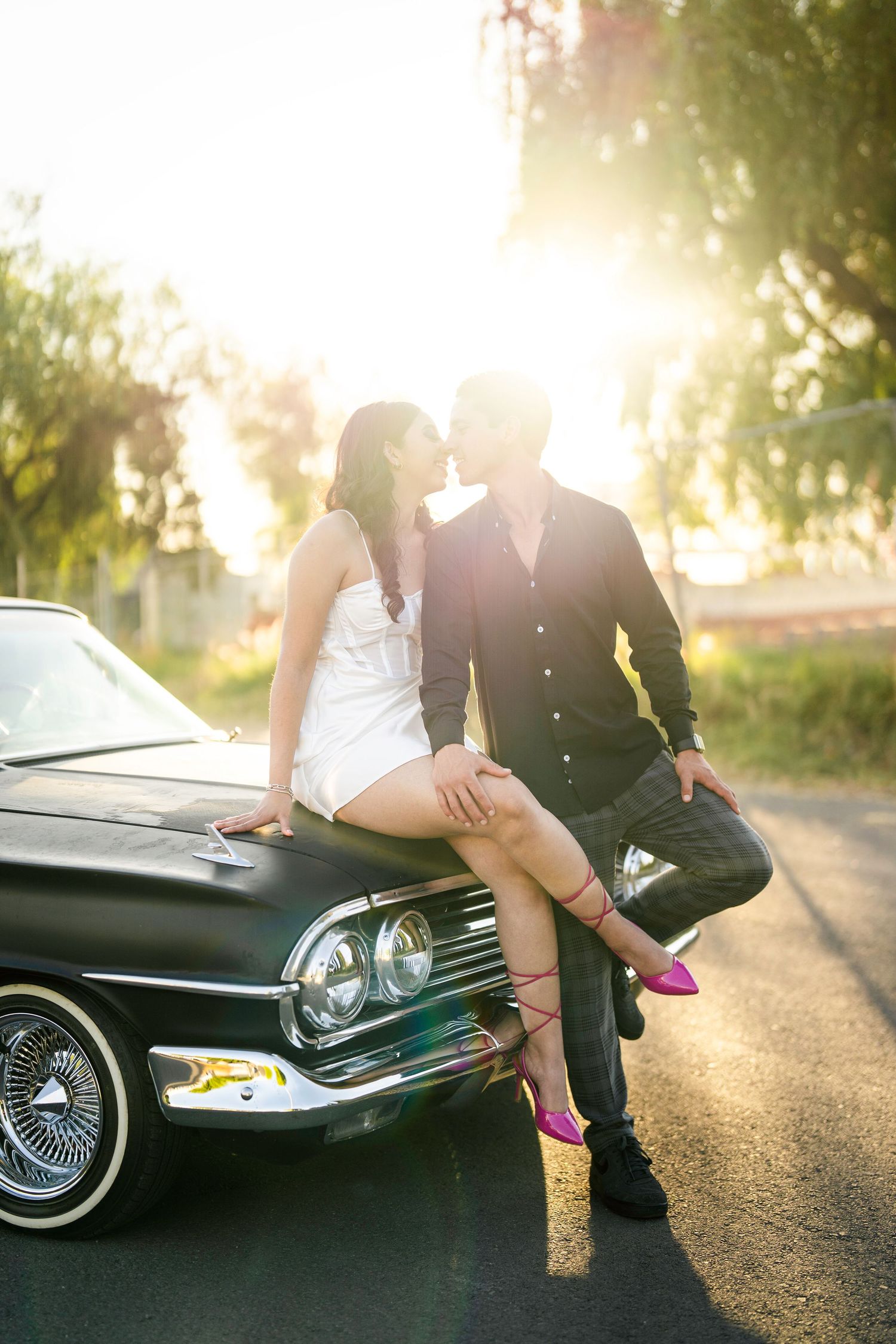 Vintage car photoshoot at sunset with silhouettes against a glowing golden background.