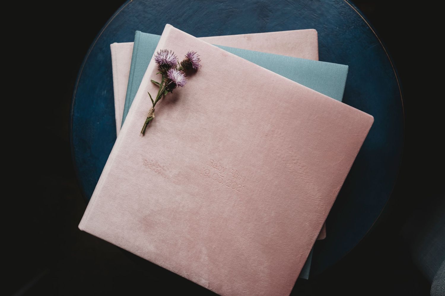 Pink photo album with dried flowers on a blue surface viewed from above.