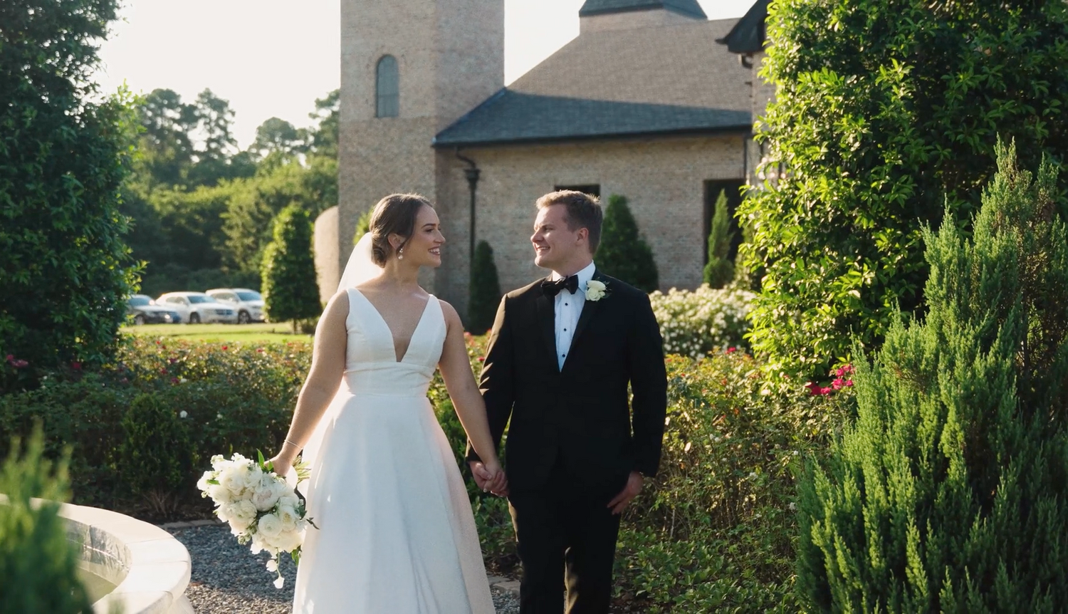 A couple in wedding attire walks together outside a stone church building on their special day.