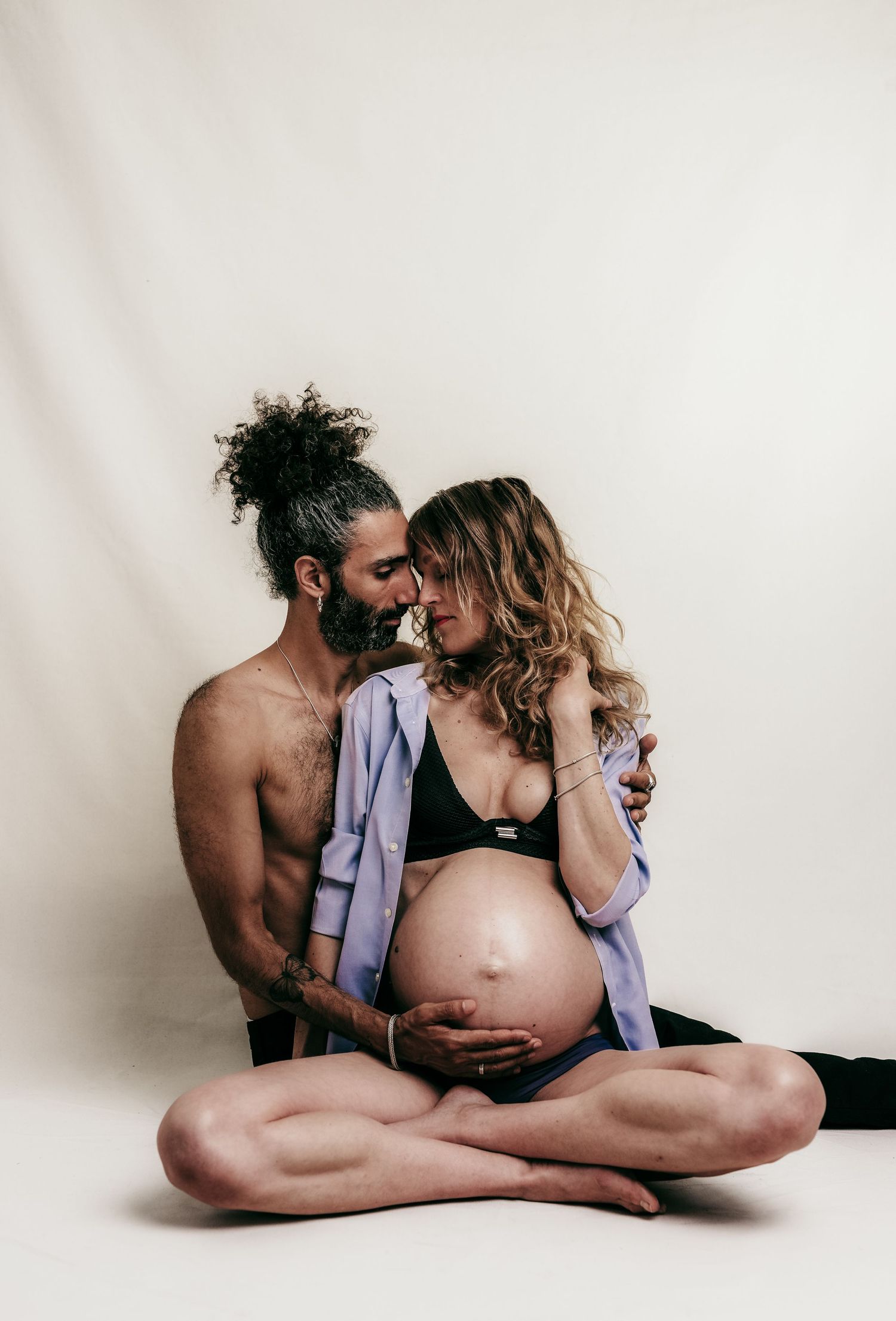 An intimate maternity photo of an expecting couple against a white backdrop.
