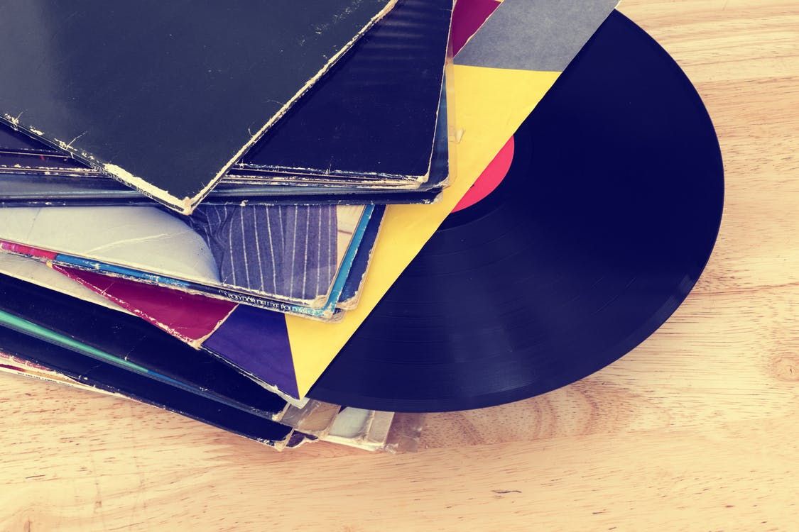 Stack of vinyl records and album covers on wooden floor with vintage filter.