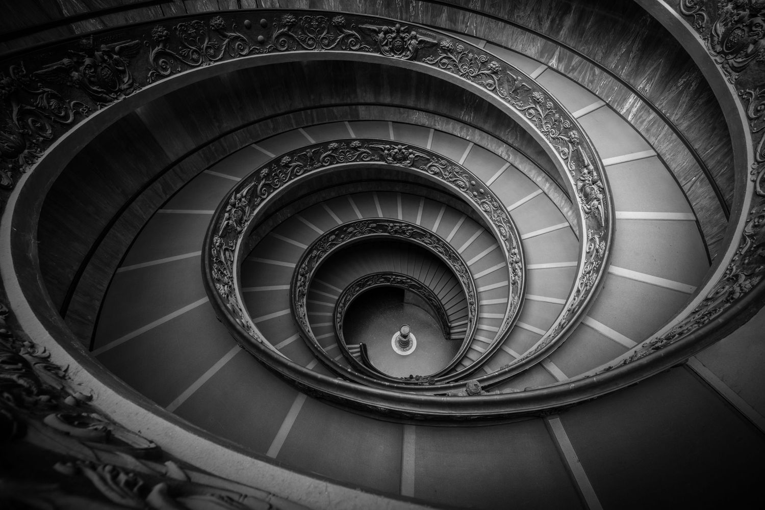 Spiral staircase in black and white creates mesmerizing circular pattern descending into darkness.