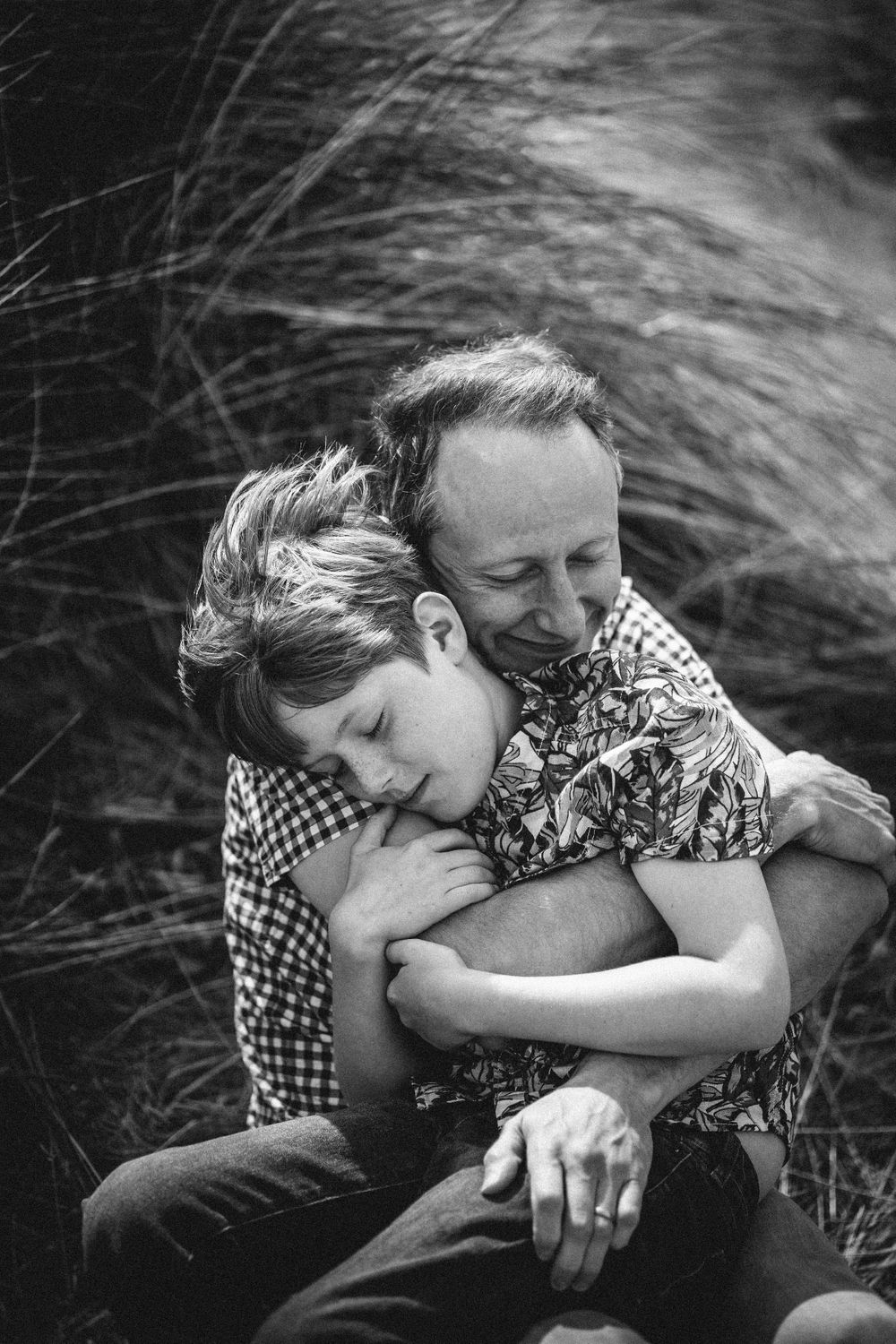 An intimate black and white portrait showing gentle embrace among wild grass.