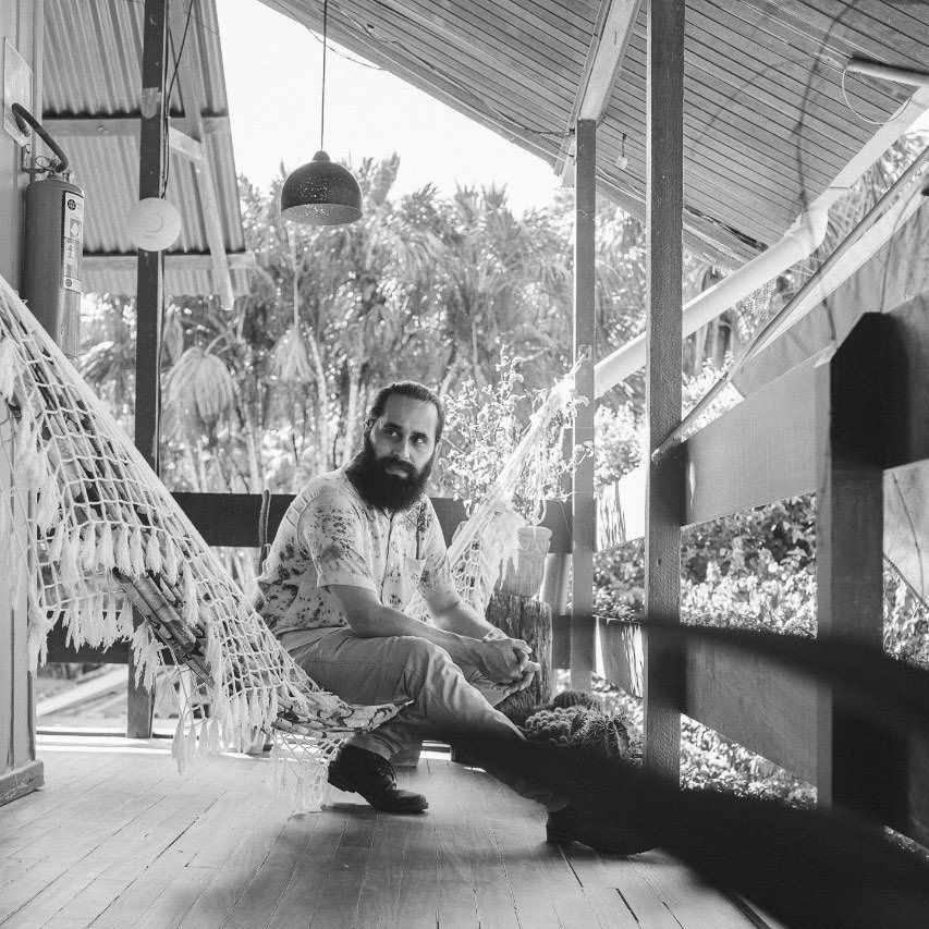 Black and white image of relaxed man sitting on porch with hammock.