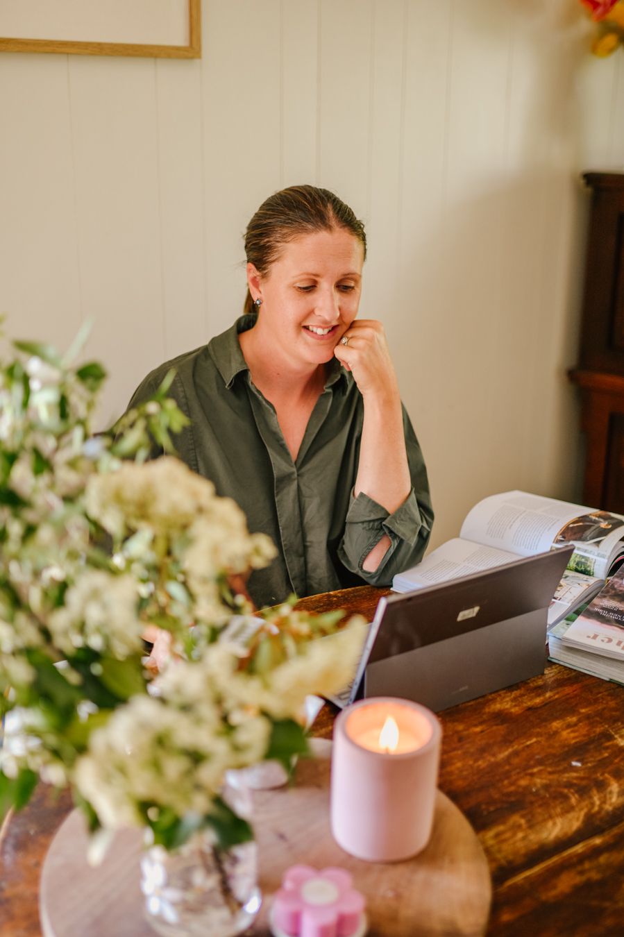 Rural women sitting at laptop at work desk with fresh cut flowers and candle