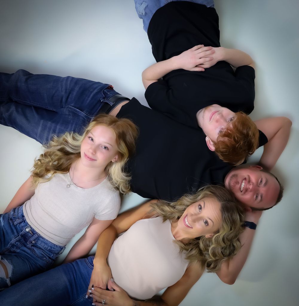 A family of four lies together in a creative studio pose against a light background.