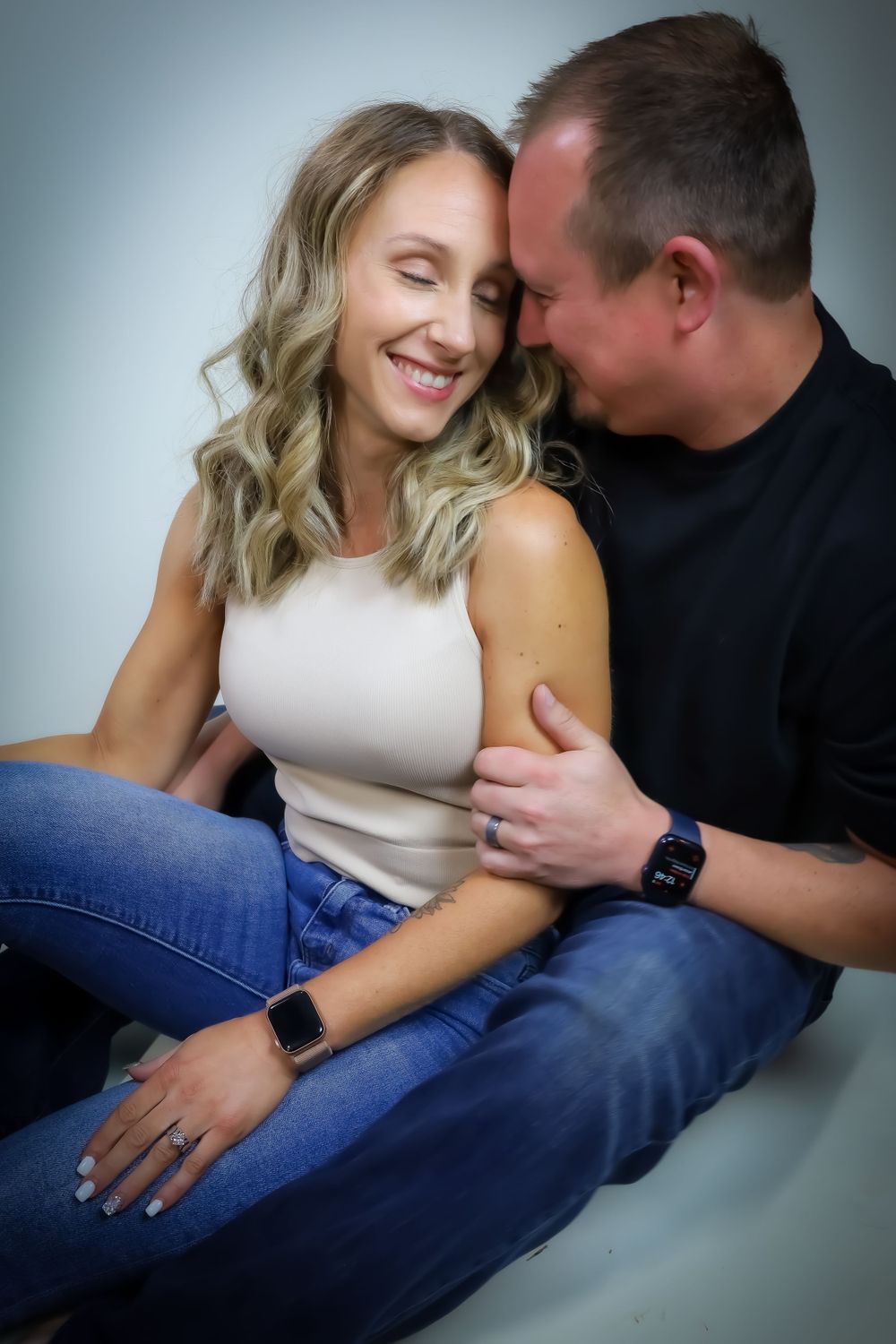 A couple shares an intimate moment while posing in casual attire against a grey background.