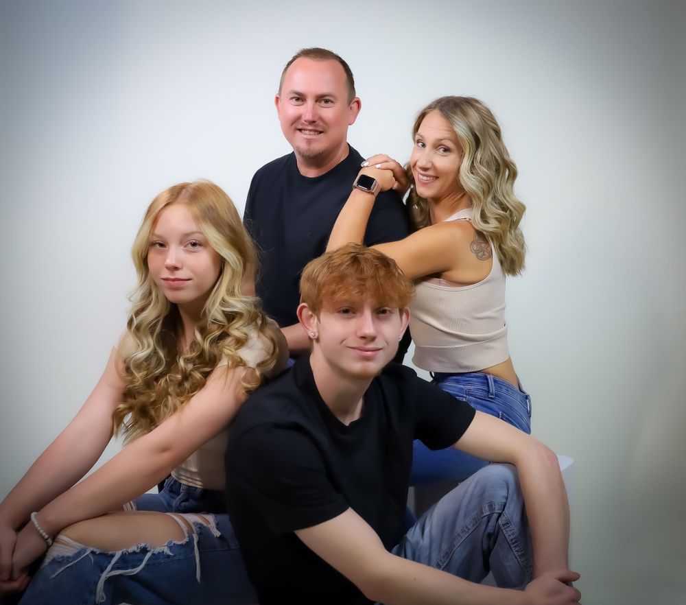A family of four poses together for a casual studio portrait against a light background.