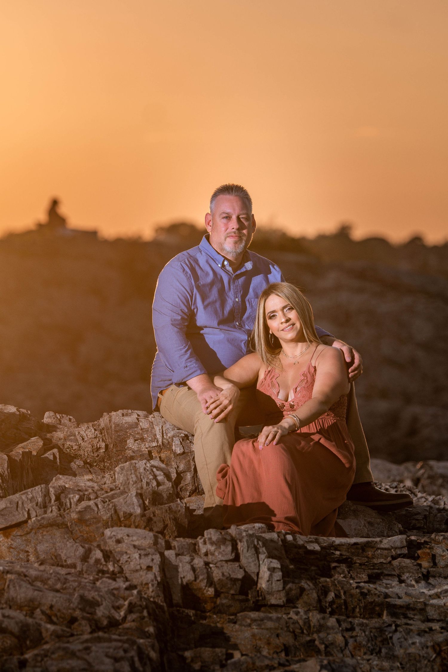 Romantic sunset portrait on rocky terrain with warm orange sky.