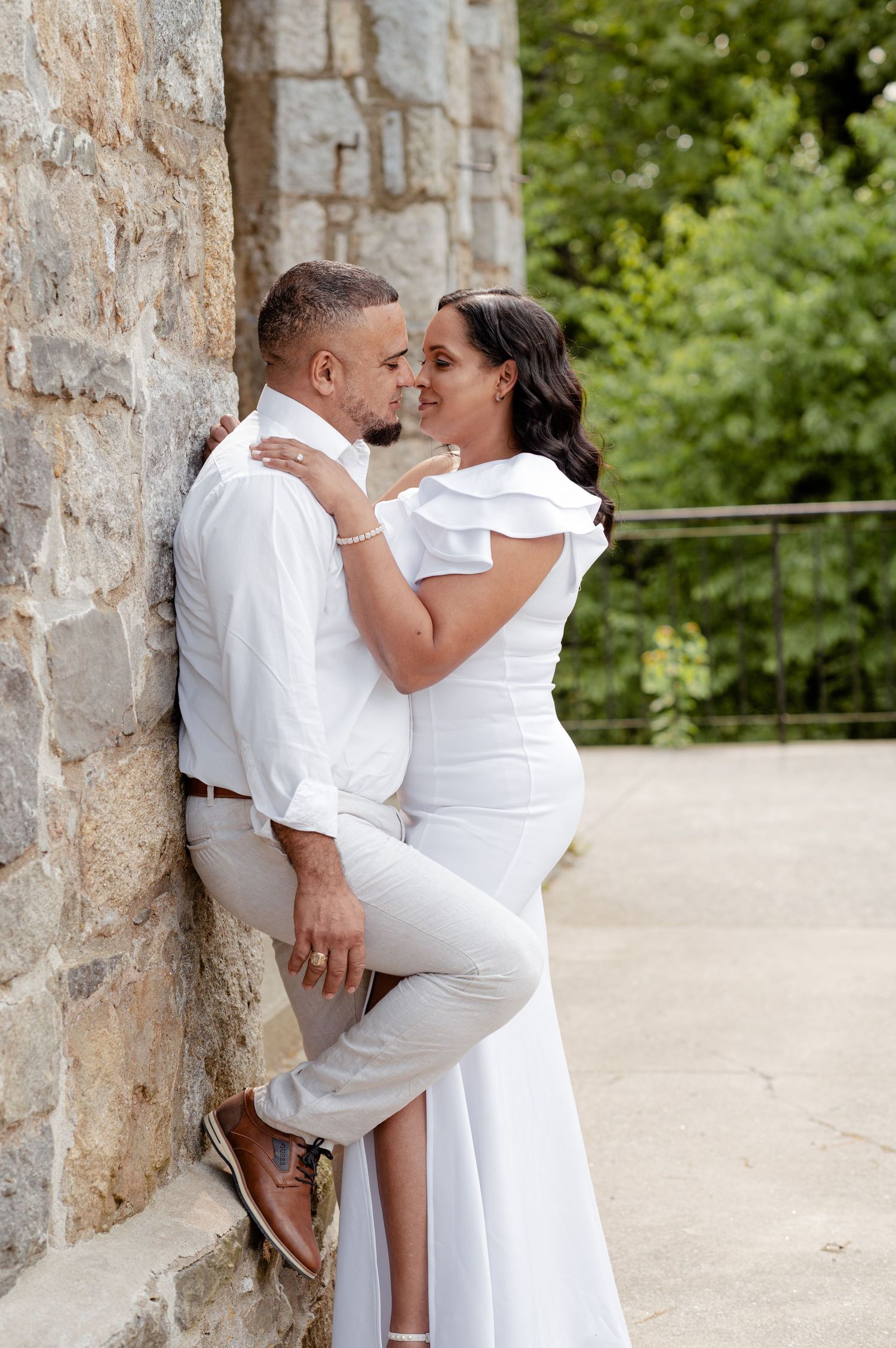 Romantic couple photoshoot against stone wall backdrop wearing all white outfits.