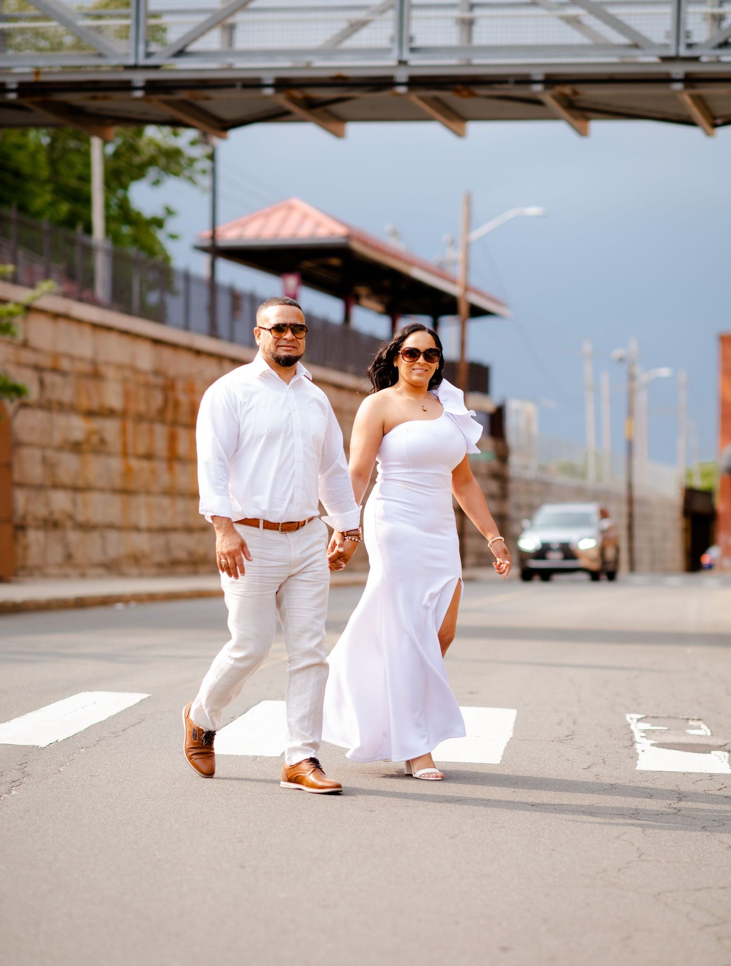 Casual couple photoshoot in white outfits on urban boardwalk setting.