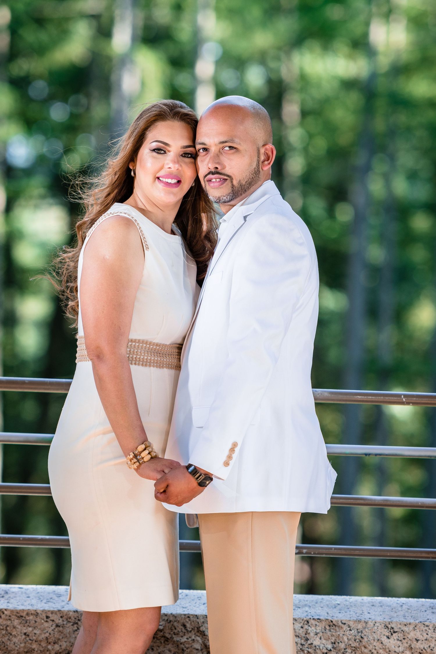A couple in coordinating white outfits poses together on an outdoor deck.
