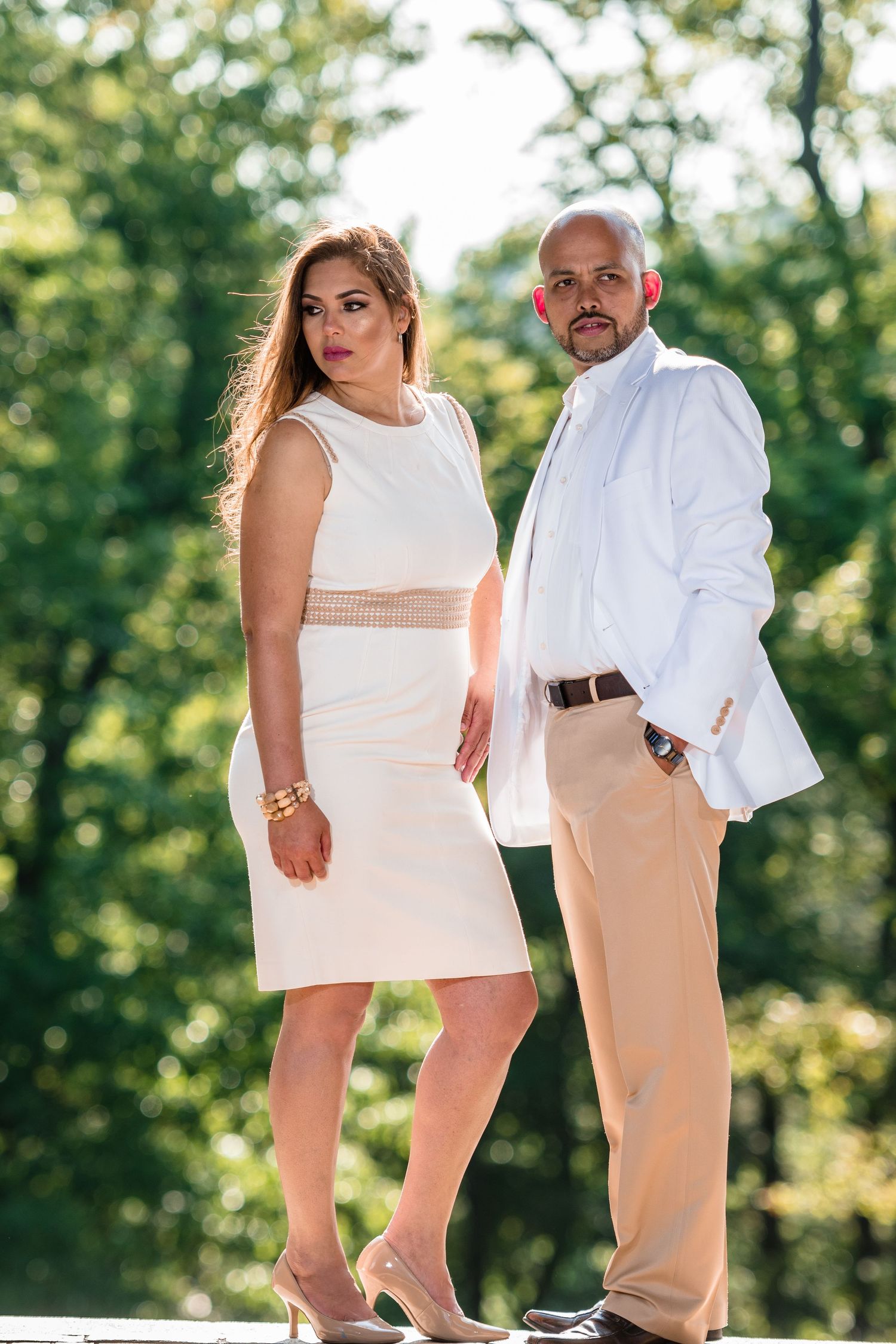 A couple in matching cream and white outfits poses elegantly outdoors.