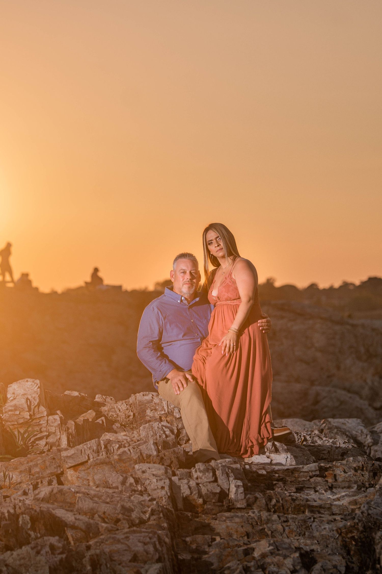Couple posing on rocky outcrop during golden sunset.